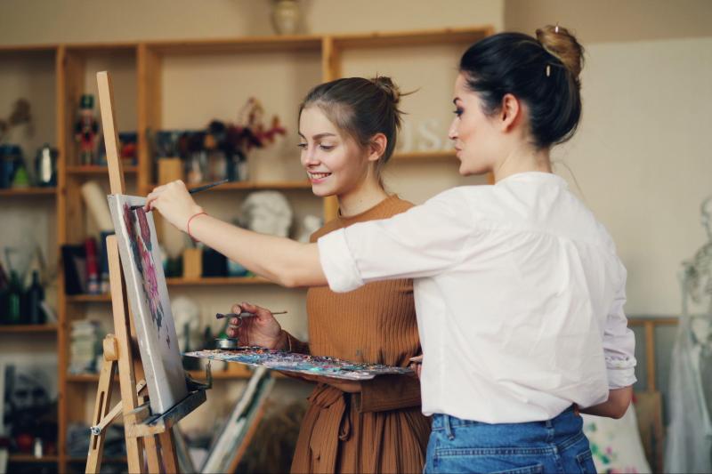 Two young women engaged in painting in a well-lit art studio.