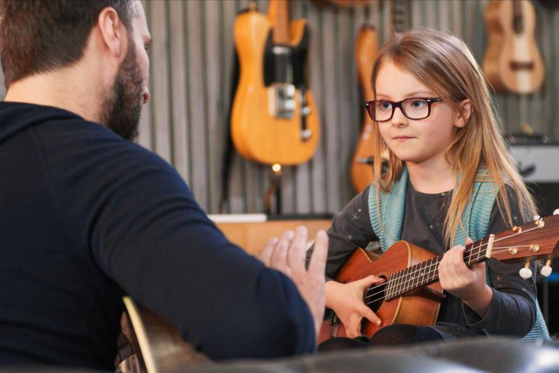 Music teacher teaching guitar lesson to child in New Zealand studio