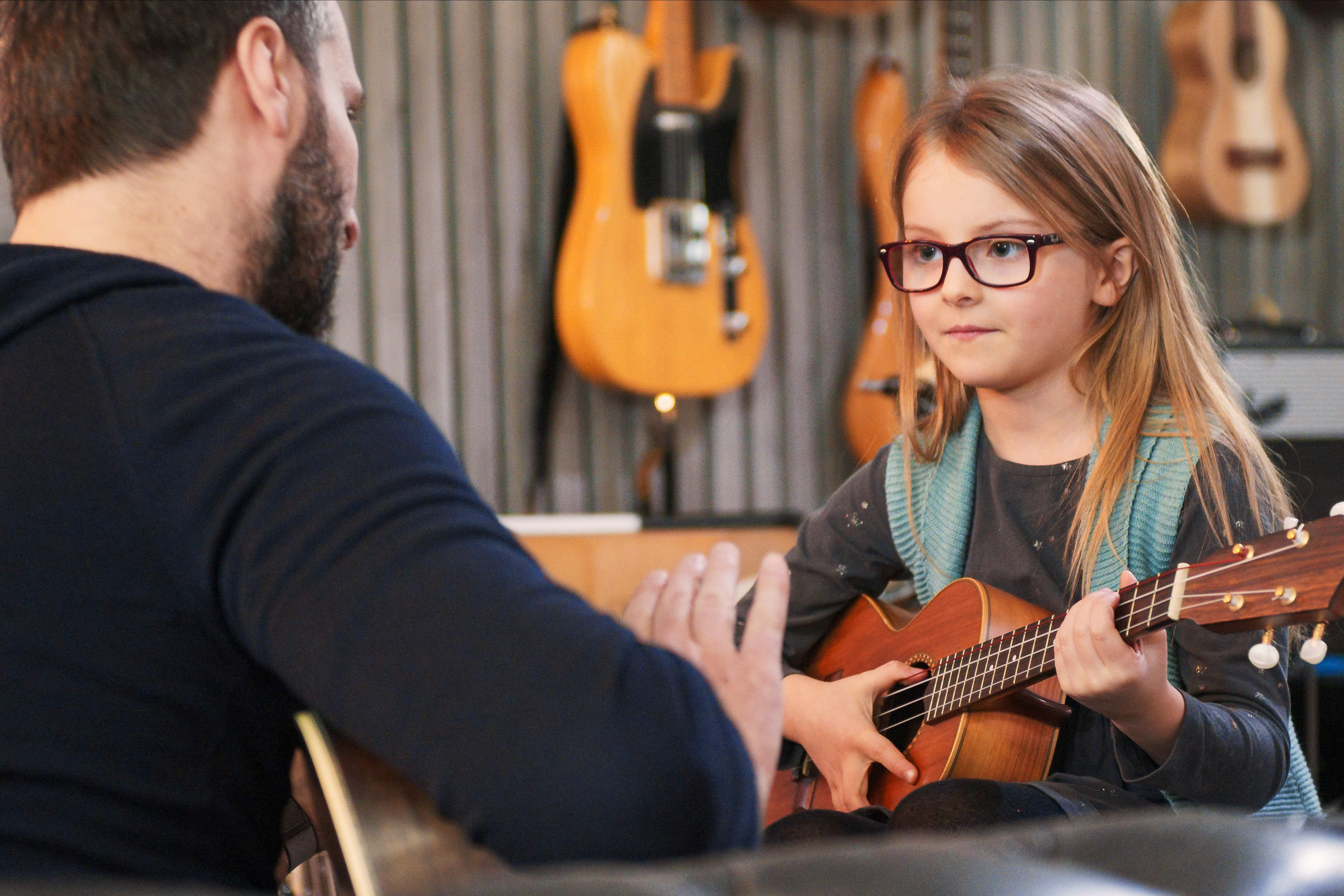 Music teacher teaching guitar lesson to child in New Zealand studio