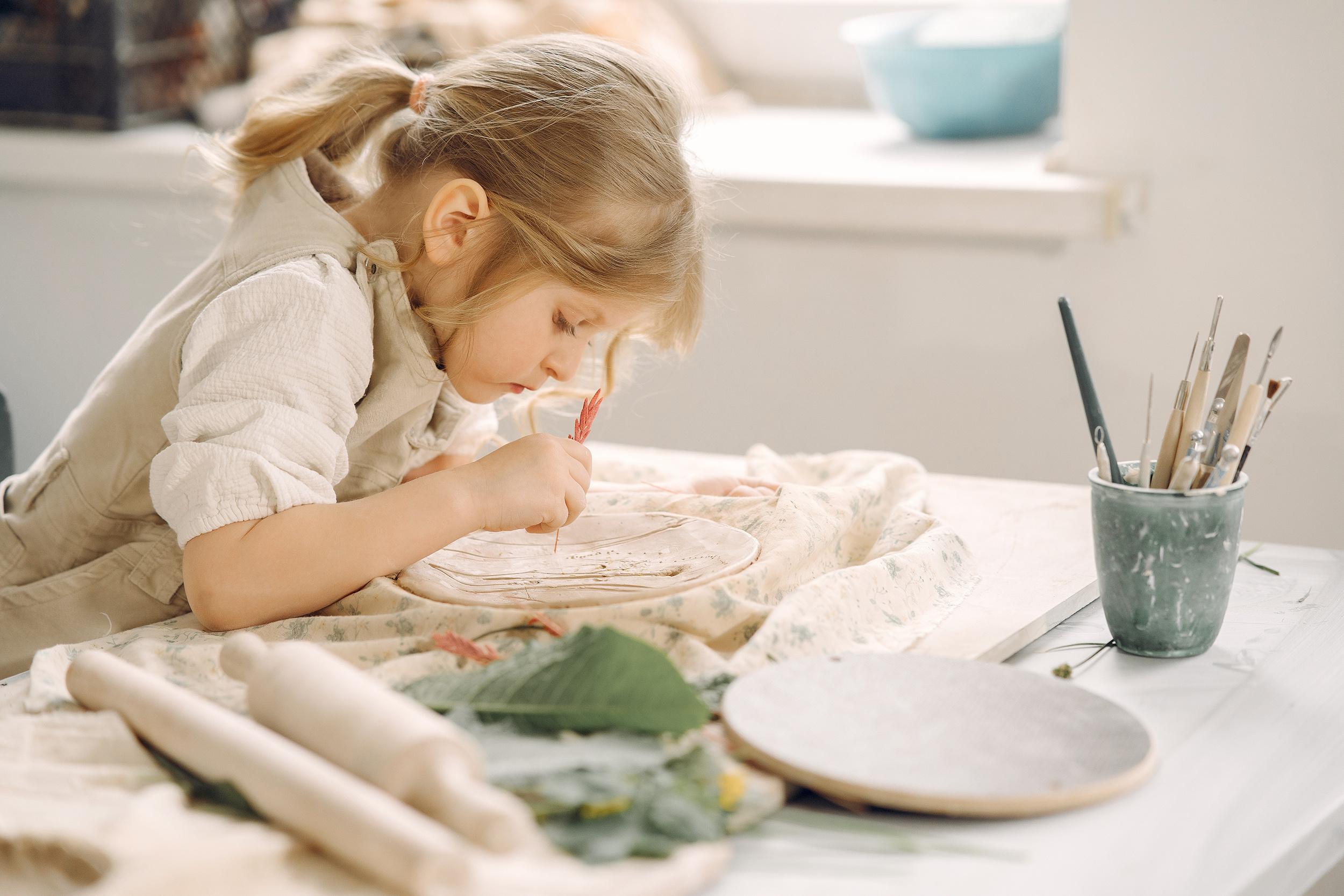 Little girl making a clay plate decoration during a creative school holiday art programme in Wellington.