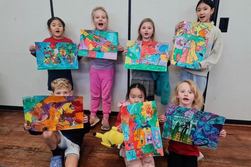 Children proudly displaying colourful paintings created during a Creative Matters art class in Auckland.