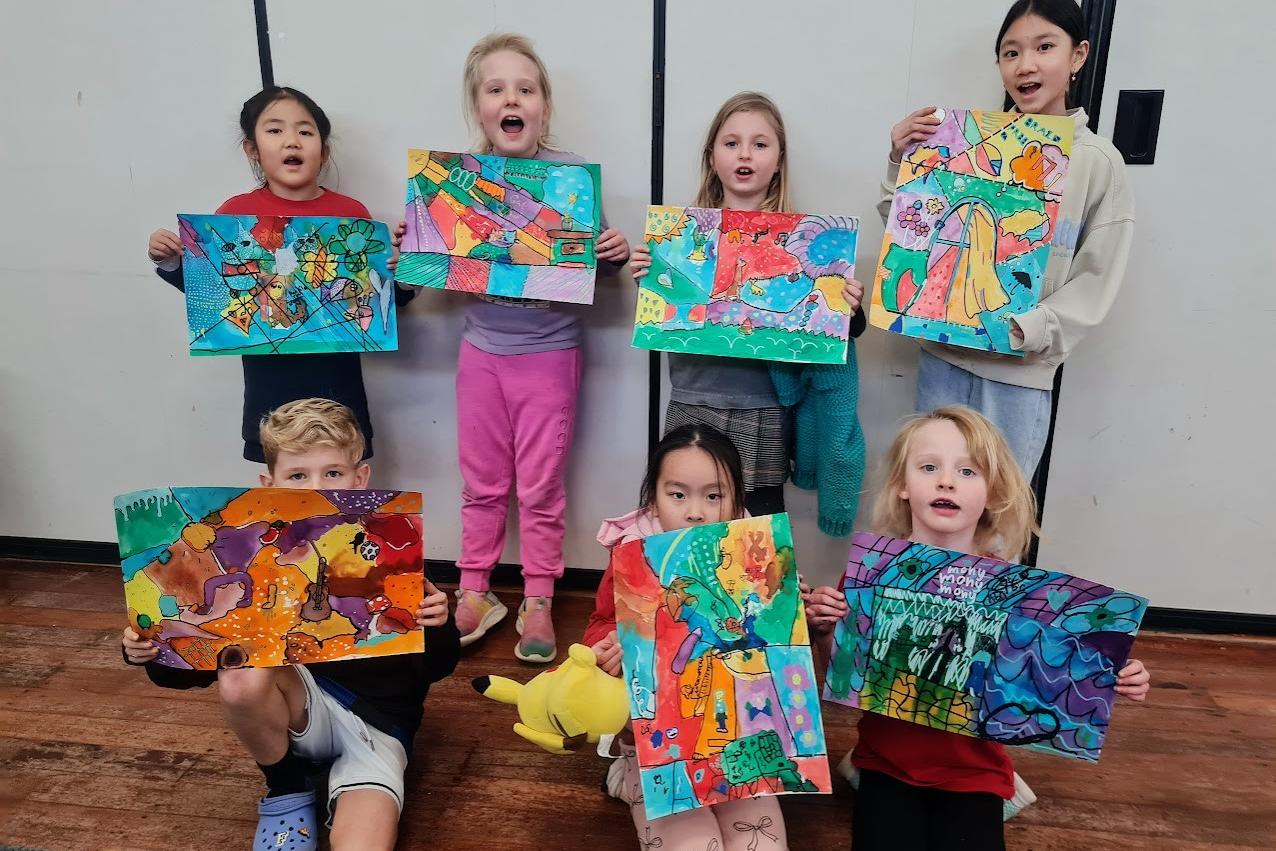 Children proudly displaying colourful paintings created during a Creative Matters art class in Auckland.