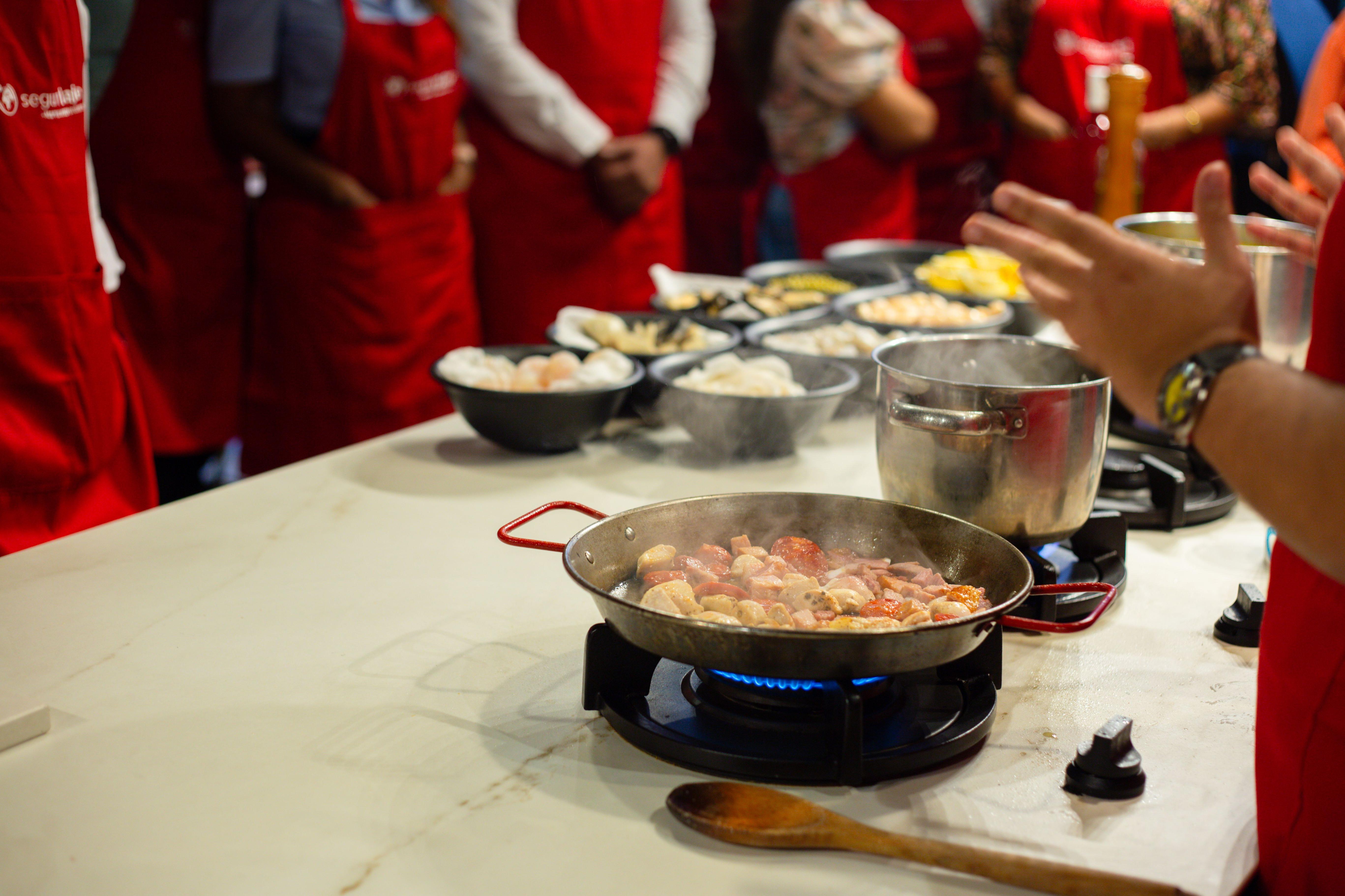 People learning cooking techniques during a hands-on class, with ingredients and a frying pan on the kitchen counter.
